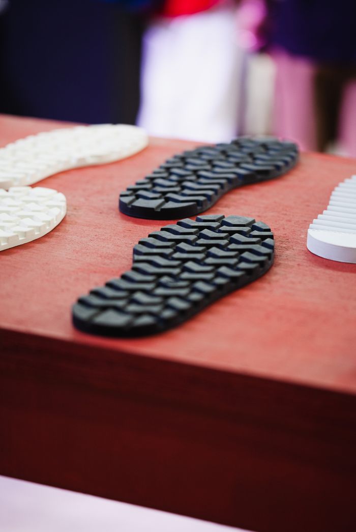 services-04 Close-up of textured rubber shoe soles displayed on a red surface with a blurred background.