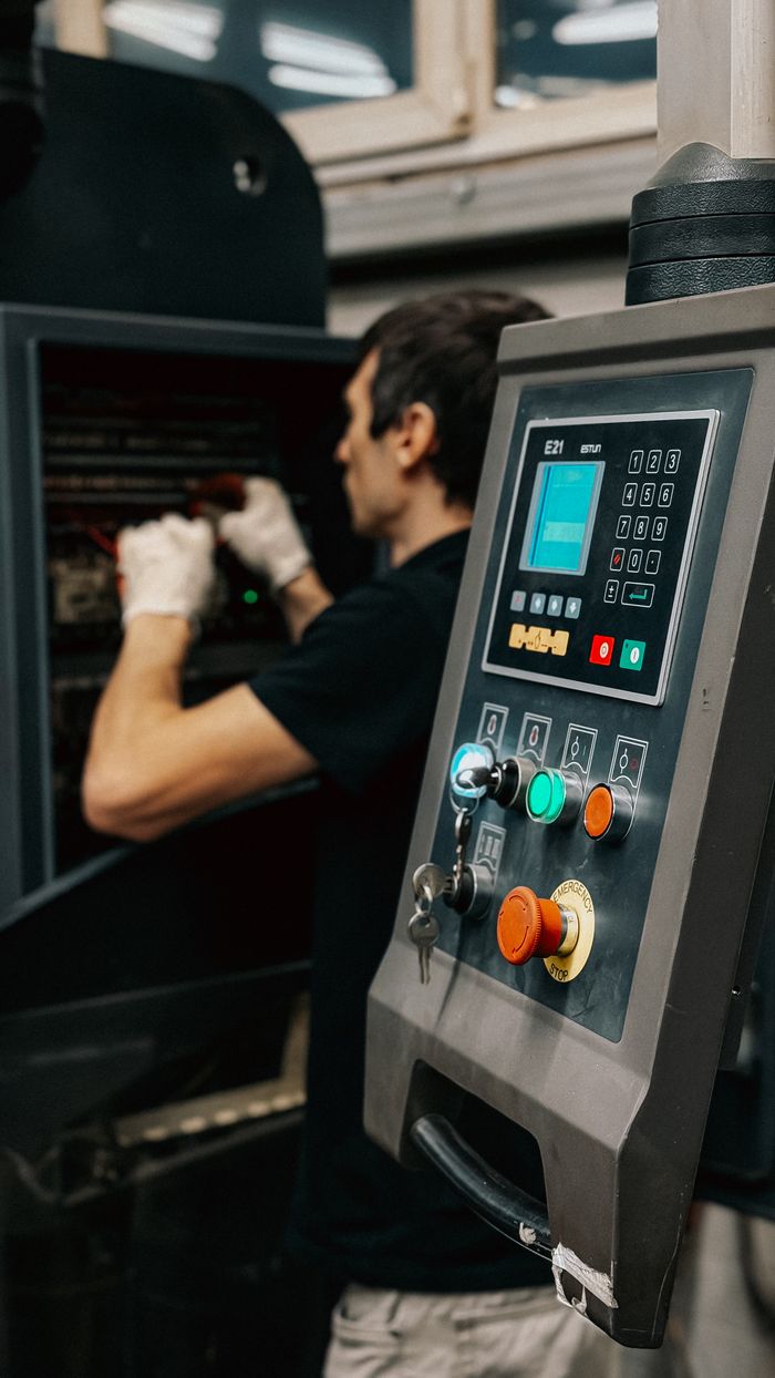why-choose-us-03 Technician using a control panel to manage machinery operations in a factory.