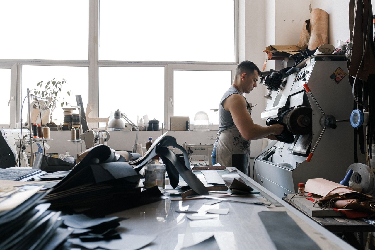 hero-01 A craftsman working with industrial machinery in a leather workshop, focused and detailed.