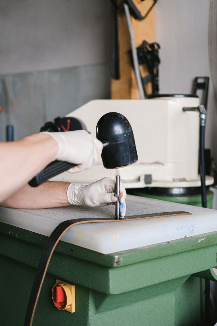 services-05 Leather artisan using a mallet to craft a belt in a workshop setting. Close-up view of hands.